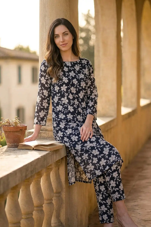 Smiling model sitting on a stone balcony ledge wearing the Midnight Blossom 2 piece allover printed lawn suit by Dorikhas.